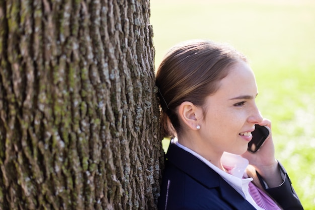 Free photo businesswoman with mobile phone resting on a tree