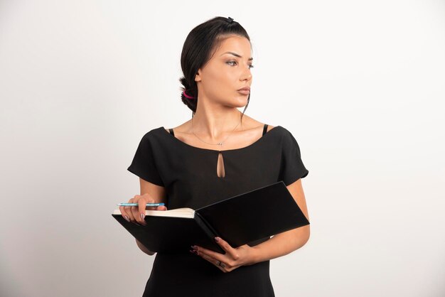 Businesswoman with notebook posing on white wall.