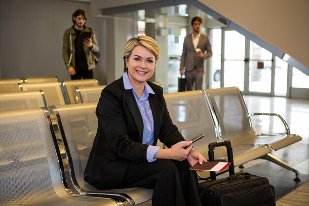 Businesswoman with passport, boarding pass and luggage sitting in waiting area