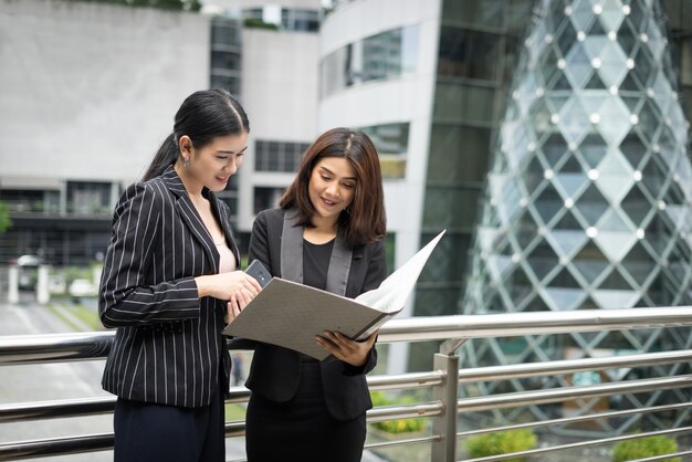 Businesswomen discussing over paperwork together against railing. Business people concept.