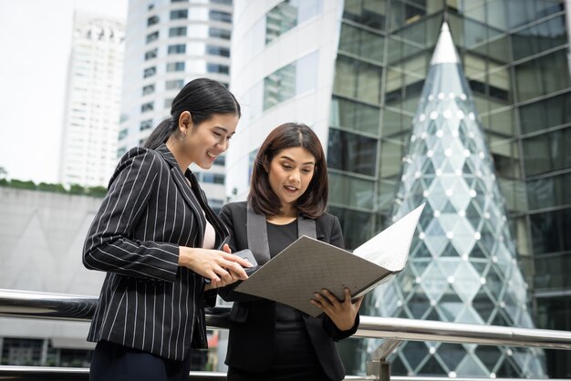 Businesswomen discussing over paperwork together against railing. Business people concept.