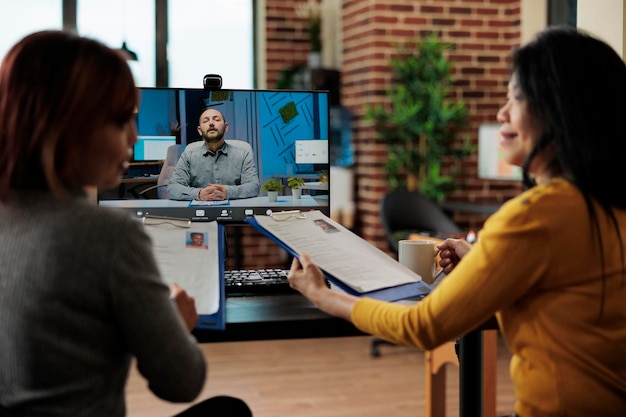 Businesswomen holding clipboard reading recruiter cv discussing company hiring plan during job appointment during online videocall meeting conference in startup office. Teleconference call