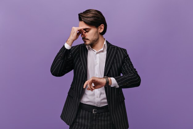 Busy exhausted man with dark hair, light shirt and striped suit thinking about something after looking at watch