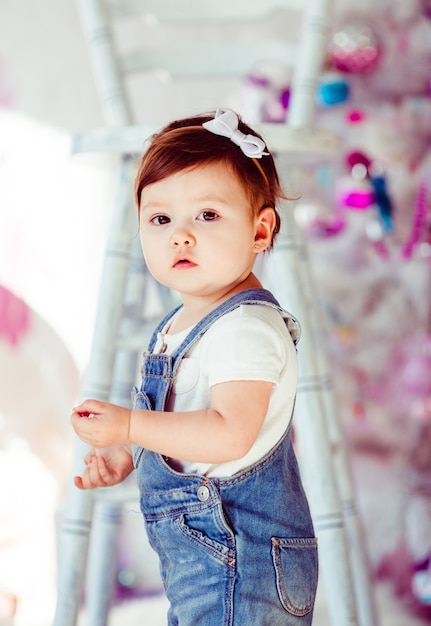 Free photo busy little girl in jeans jumpers stands before tall white chair