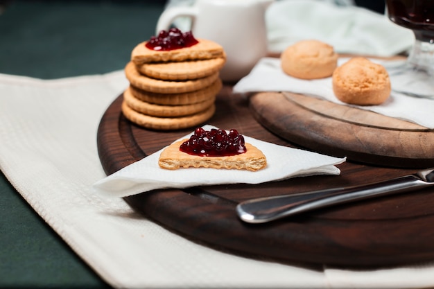 Butter cookies with strawberry jam on a wooden board on a piece of tissue