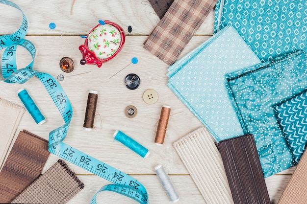 Buttons; a set of needles; thread reels are needed for sewing clothes on wooden table