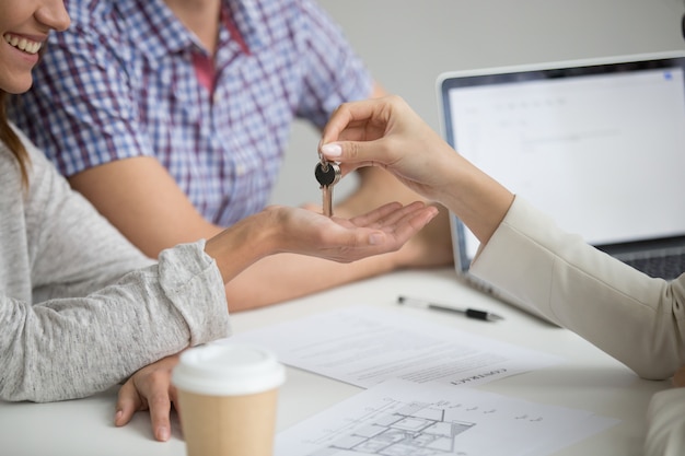 Buying new house concept, realtor giving keys to couple, closeup