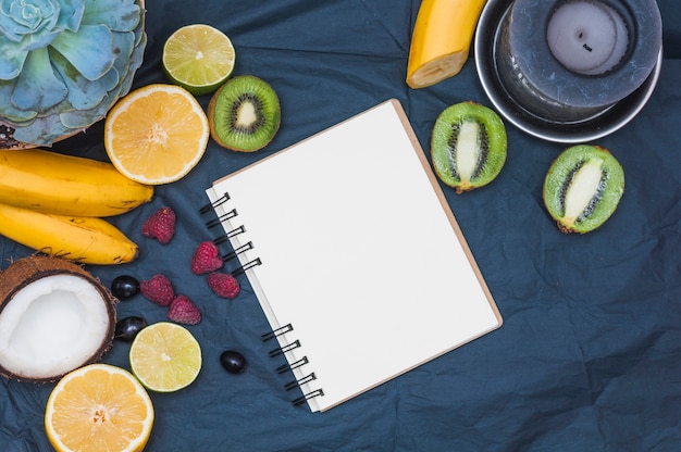 Cactus plant; fruits; coconut; candle and blank page spiral notepad on textile