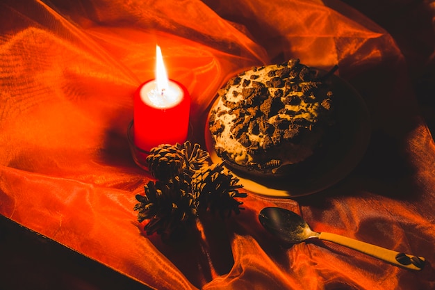 Free photo cake; lit candle and pinecones with spoon on red clothes