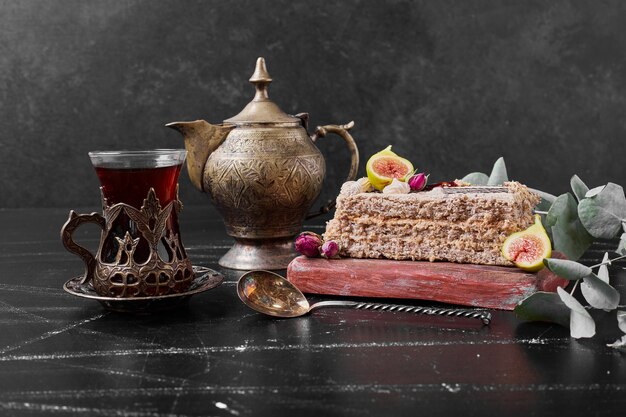 Cake slice with a glass of tea on wooden platter.