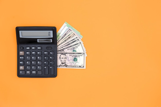 Free Photo calculator and dollar bills on an orange background copy space