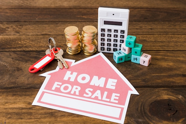 Calculator, math blocks, stacked coins and key with home for sale icon on wooden background