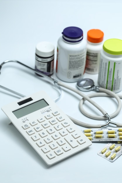 calculator, stethoscope and medicine bottles on white background