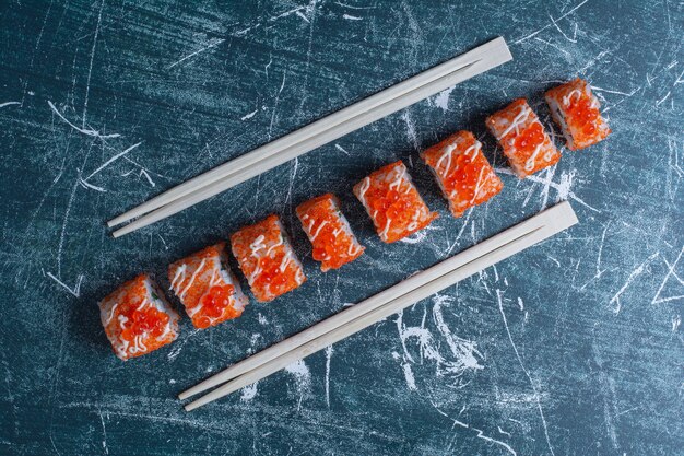 California sushi roll decorated with red caviar on blue with chopsticks.