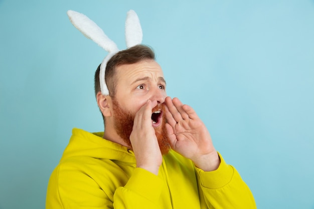 Free Photo calling, screaming. caucasian man as an easter bunny with bright casual clothes on blue studio background.