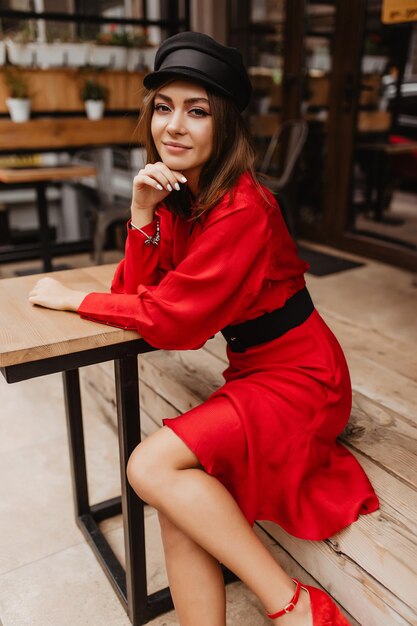 Calm girl with impressive appearance is sitting gracefully at wooden table Charming delicate model quietly poses for portrait