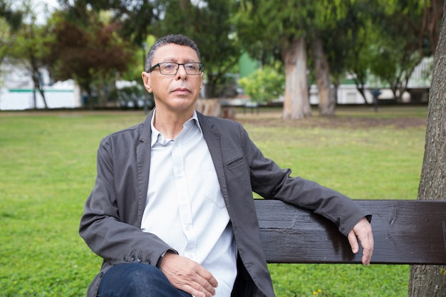 Calm middle-aged man sitting and relaxing on bench in park