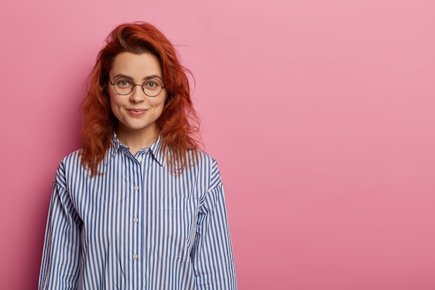 Free Photo calm optimistic red haired european woman looks directly at camera, has relaxed facial expression, charming smile