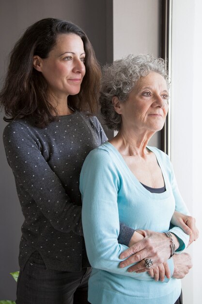 Calm pensive senior mother and her daughter looking out window