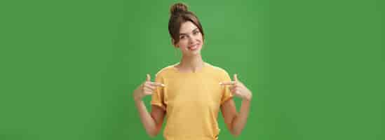 Free photo calm and polite friendlylooking skillful young female coworker in yellow tshirt pointing at herself selfassured tilting head and smiling at camera wanting participate in event over green background