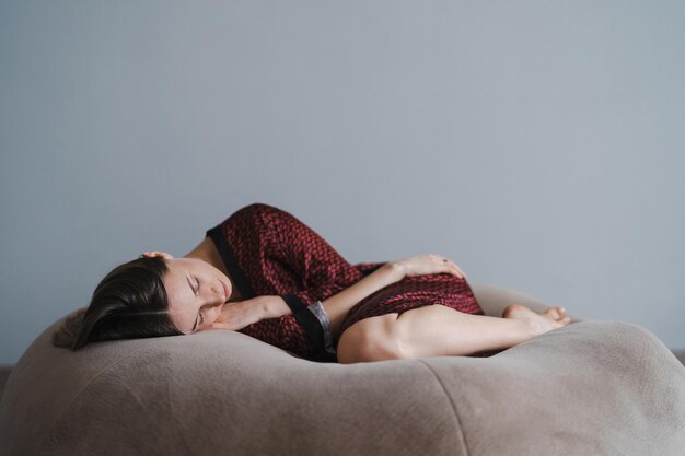 Calm serene beautiful young lady lying down in a dream relaxing sleep on a soft beige bean bag enjoying a good healthy sleep