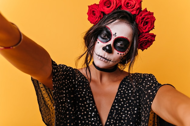 Free photo calm slender girl makes selfie, showing off her image for halloween. indoor portrait of pretty model on orange wall