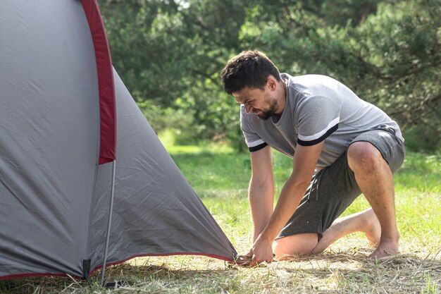 Camping, travel, tourism, hike concept - young man setting up tent in the forest.