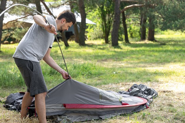 Camping, travel, tourism, hike concept - young man setting up tent outdoors.