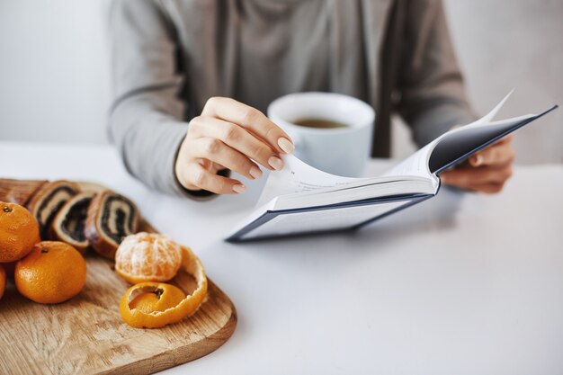 Can not wait to read whole book. Girl is in love with story written on pages of novel, having lunch, drinking tea with tangerines and rolled cake. Office worker having break after meeting with clients