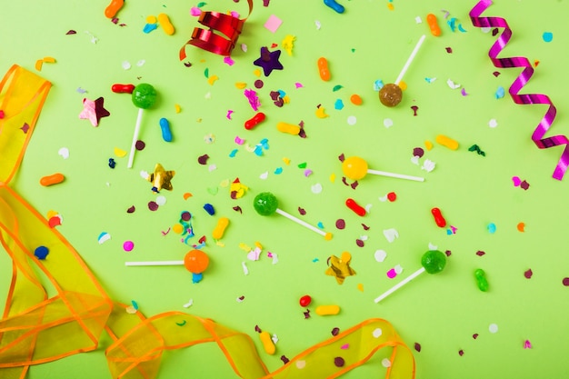 Free photo candies and lollipops with confetti and curled streamer on green background