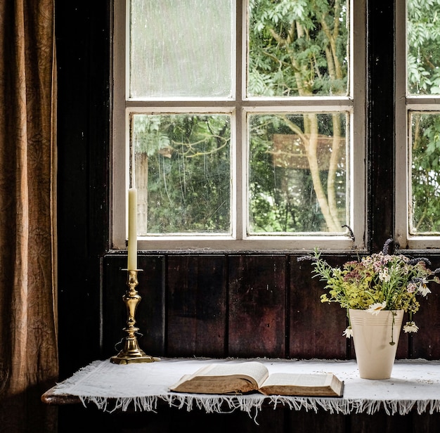 Free Photo candle put next to the flowers and a book in front of the window