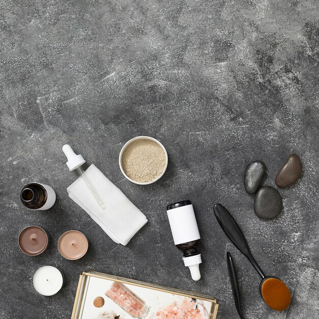 Candles; essential oil bottle; rhassoul clay; la stone; himalayan rock salt on tray against black concrete backdrop