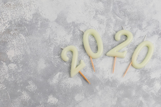 Candles in the shape of numbers 2020 as a symbol of the new year next to christmas shaped sparkle candies on a gray table. Top view, flat lay