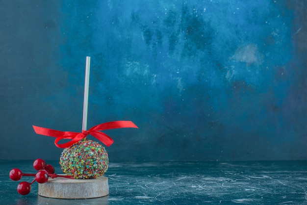 Free Photo a candy coated lollipop and christmas berry ornament on a piece of wood on blue background. high quality photo