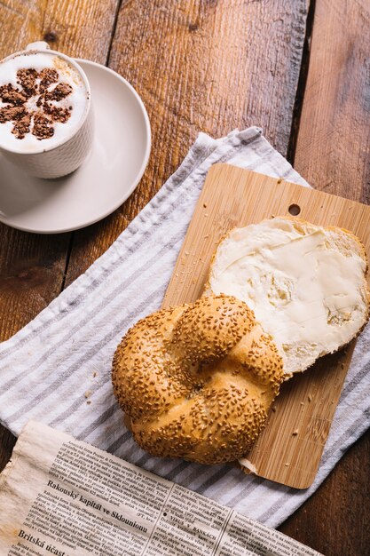 Cappuccino coffee and bread slice with cheese on chopping board over the table