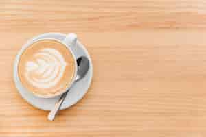 Free photo cappuccino coffee with art latte and spoon on wooden background