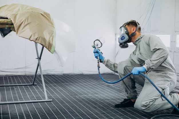 Car mechanic painting car with spray gun