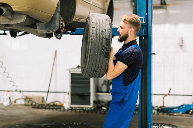 Free photo car mechanic placing auto wheel on transport nave