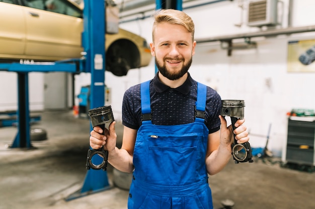 Car mechanic in uniform handling engine pistons