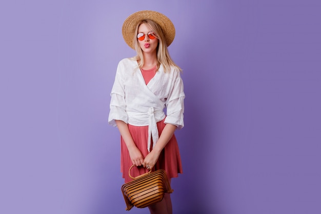 Free photo carefree brunette woman in trendy pink dress and straw hat holding bamboo bag on violet.