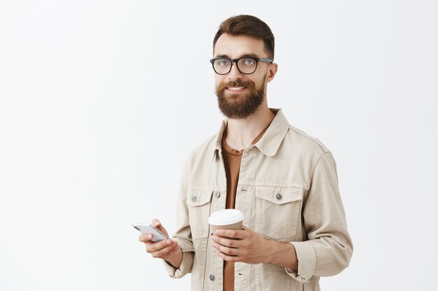 Carefree handsome bearded man in glasses posing against the white wall