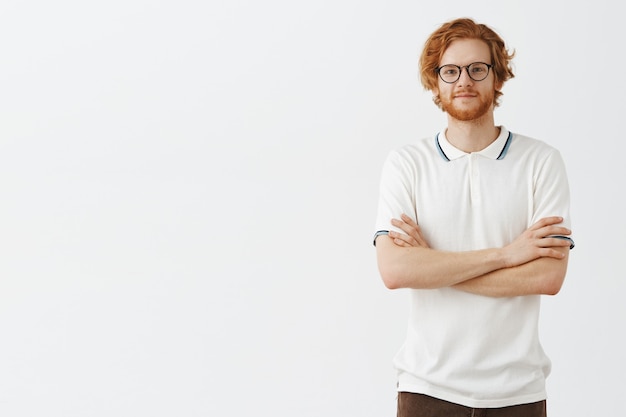 Free photo carefree handsome bearded redhead guy posing against the white wall with glasses