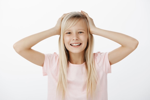 Carefree happy little daughter with blond hair in pink t-shirt, holding hands on head and smiling from satisfaction and happy attitude, liking new group and hanging out with friends during lunch