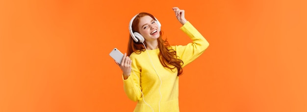 Free Photo carefree happy redhead teenage girl receive new headphones for christmas gift dancing lift hand up w