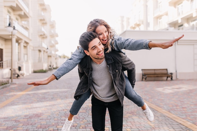 Free photo carefree man in black jacket walking around with girl. outdoor portrait of blissful couple enjoying weekend together.