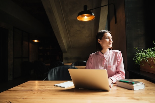 Carefree pensive woman sitting by the table in cafe