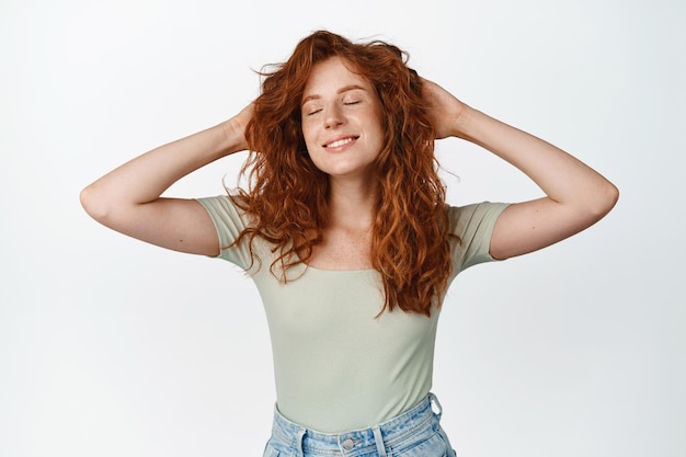 Free Photo carefree redhead girl with natural healthy red hair holding hands behind head and resting lying with pleased smile and closed eyes standing over white background