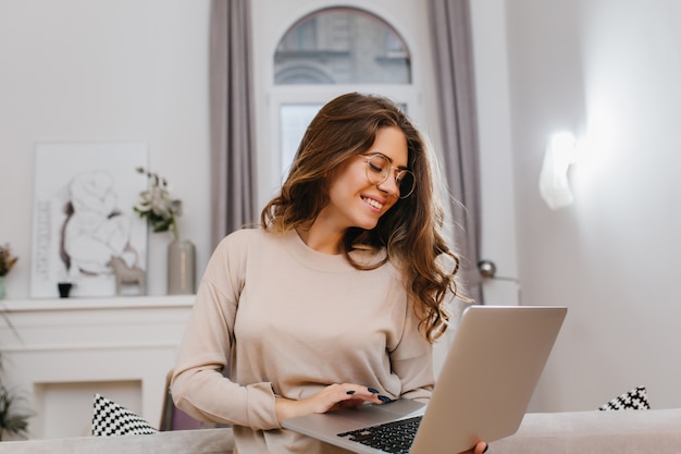 Carefree smart girl in beige shirt posing with romantic smile, working with computer