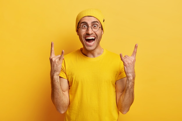 Free Photo carefree smiling positive man makes rock n roll gesture, enjoys cool music, lauhgs happily