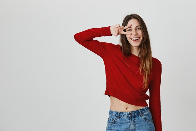 Carefree smiling woman in cropped top show peace sign over eye